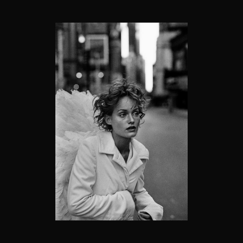 A woman in a light coat with angel wings on her back, on a city street