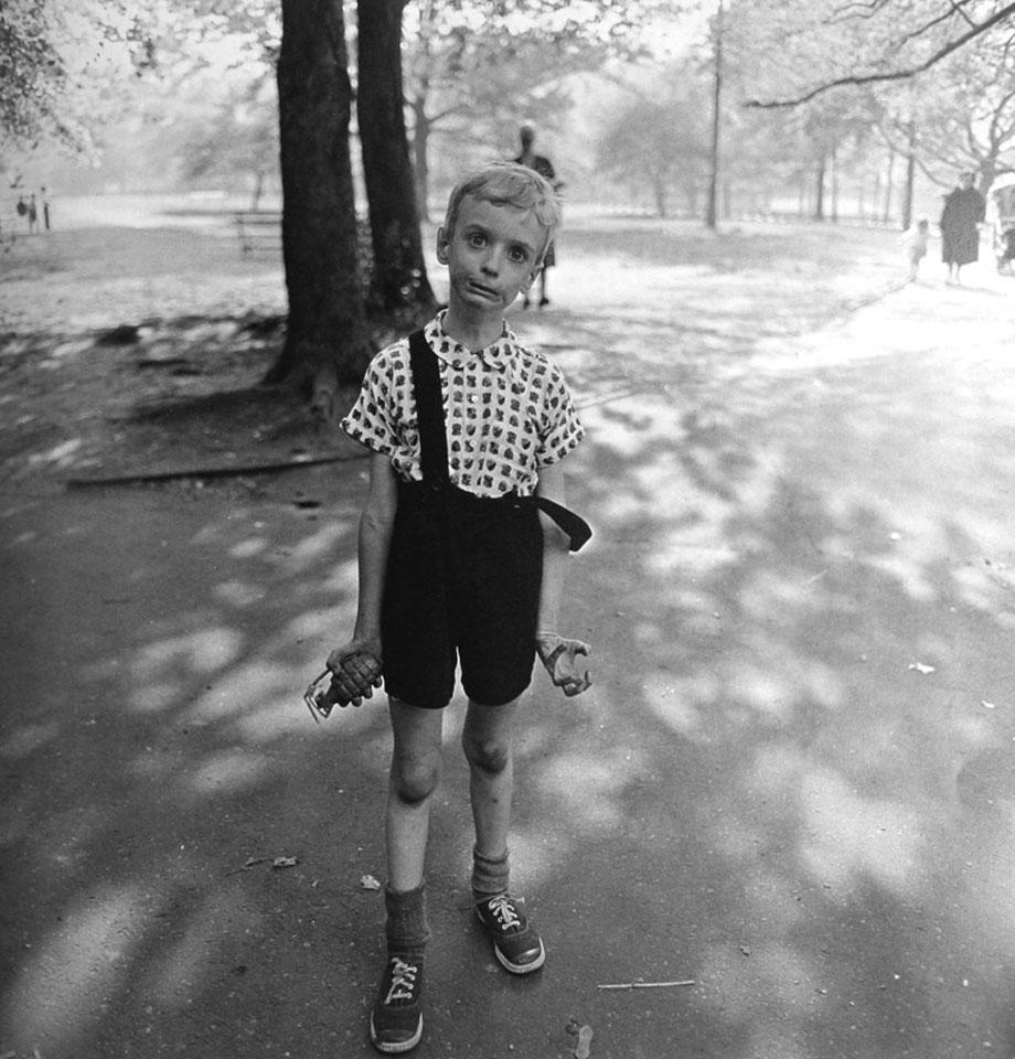 A thin boy grimacing and holding a toy hand grenade in Central Park, photograph by Diane Arbus