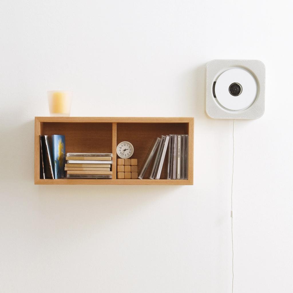 MUJI CD player on a white wall shelf next to a wooden disc storage box