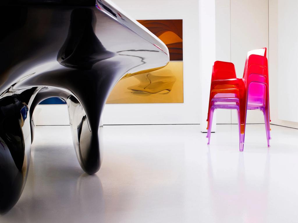 A black streamlined table and a stack of transparent pink chairs in a white gallery