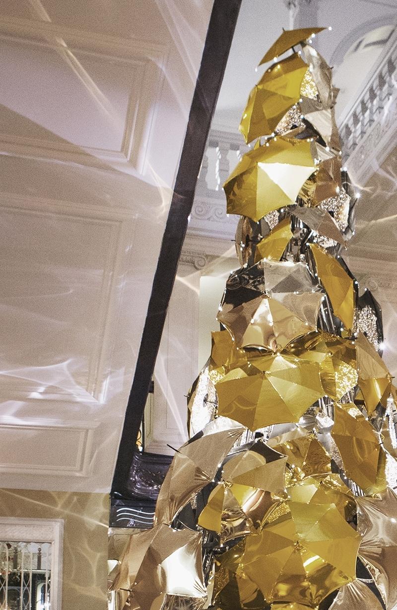 Gold and silver umbrellas arranged in the shape of a Christmas tree beside the hotel's dark staircase