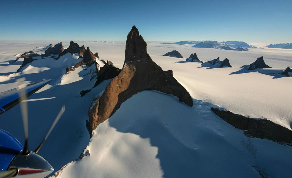An aerial view of sharp rocky peaks rising above the snowy Antarctic plains