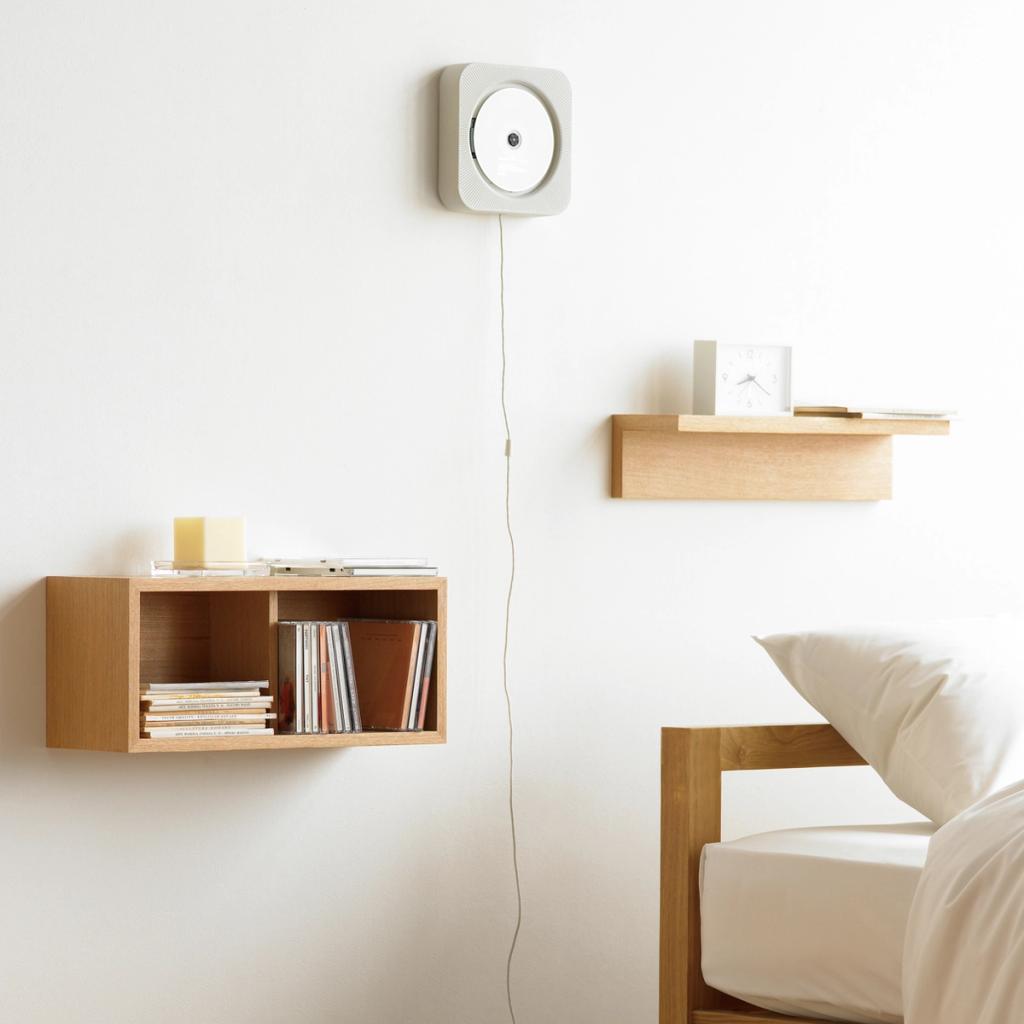 MUJI CD player on a white wall above a wooden shelf of discs by a bed