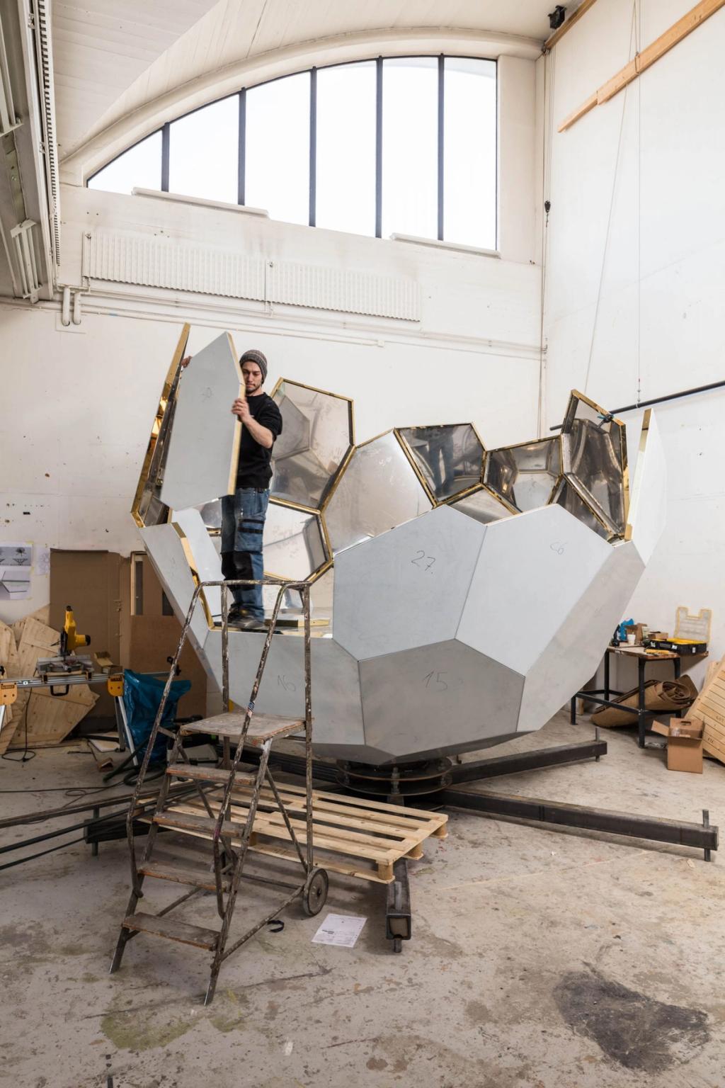 A worker assembling the mirrored panels of the Solar Egg sauna's frame in the workshop