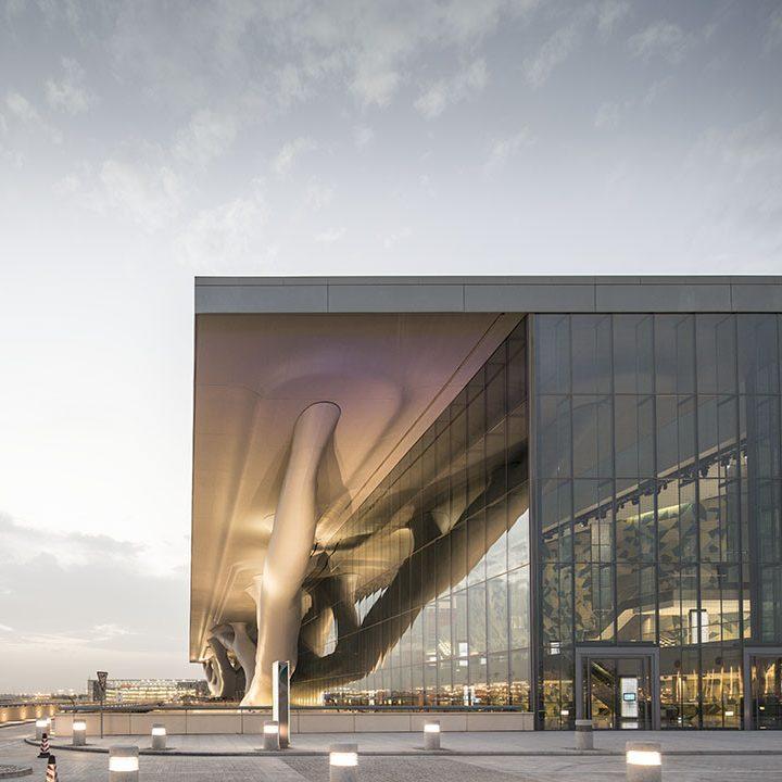 The entrance to the National Convention Centre in Doha, featuring a branching support column and full-height glazing