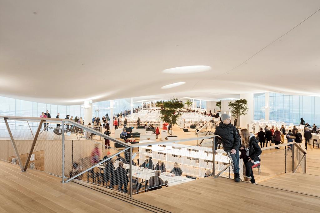The open reading room at Oodi with its undulating white ceiling, light wooden floor and visitors