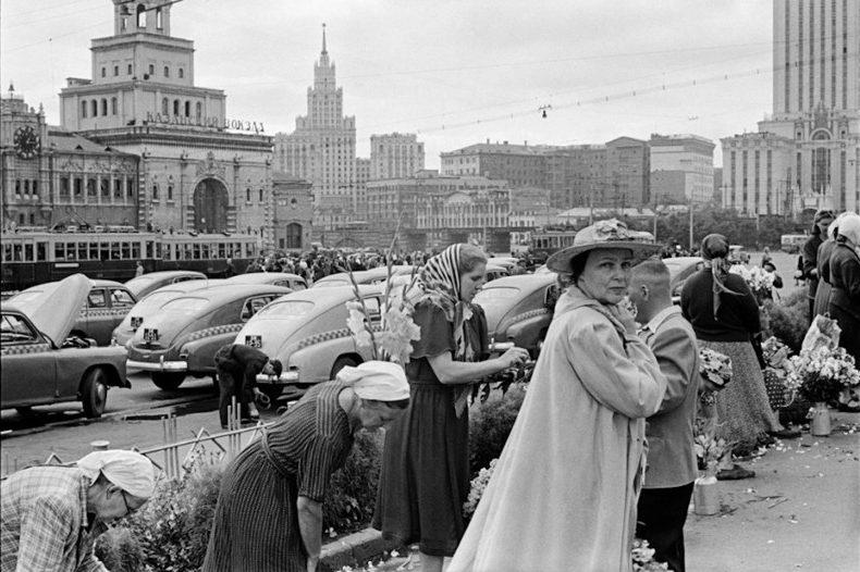 The flower market near Leningradsky Station in Moscow; a woman in a light-coloured coat glances back over her shoulder