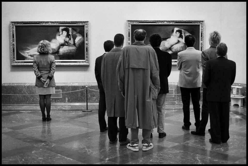 A woman and a group of men examining Goya's The Clothed Maja and The Nude Maja at the Museo del Prado