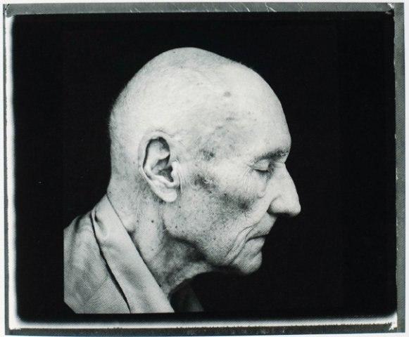 A profile portrait of an elderly bald man with closed eyes against a black background