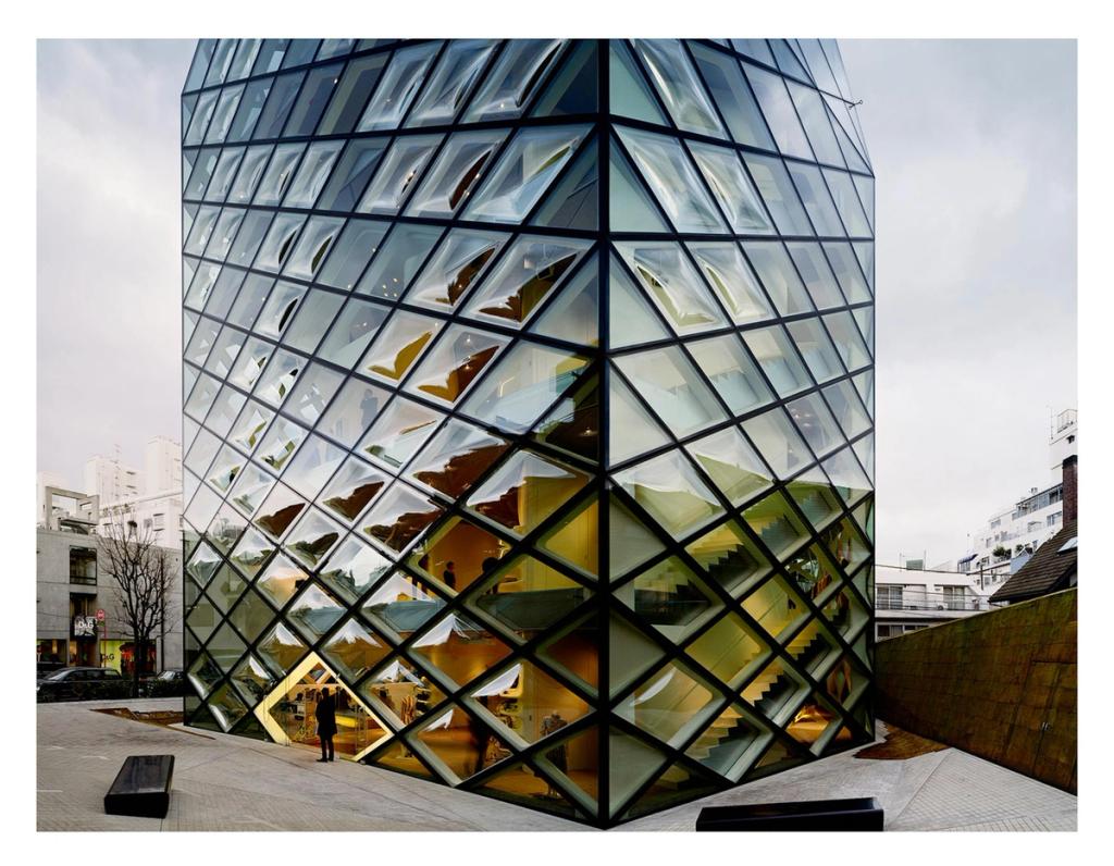 A glass building façade with a diamond-lattice grid; a human figure visible at the corner