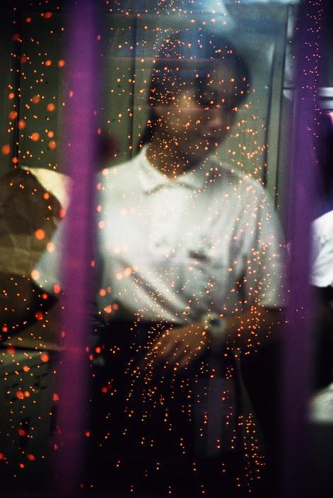 A blurred silhouette of a person behind glass scattered with orange sparks of light