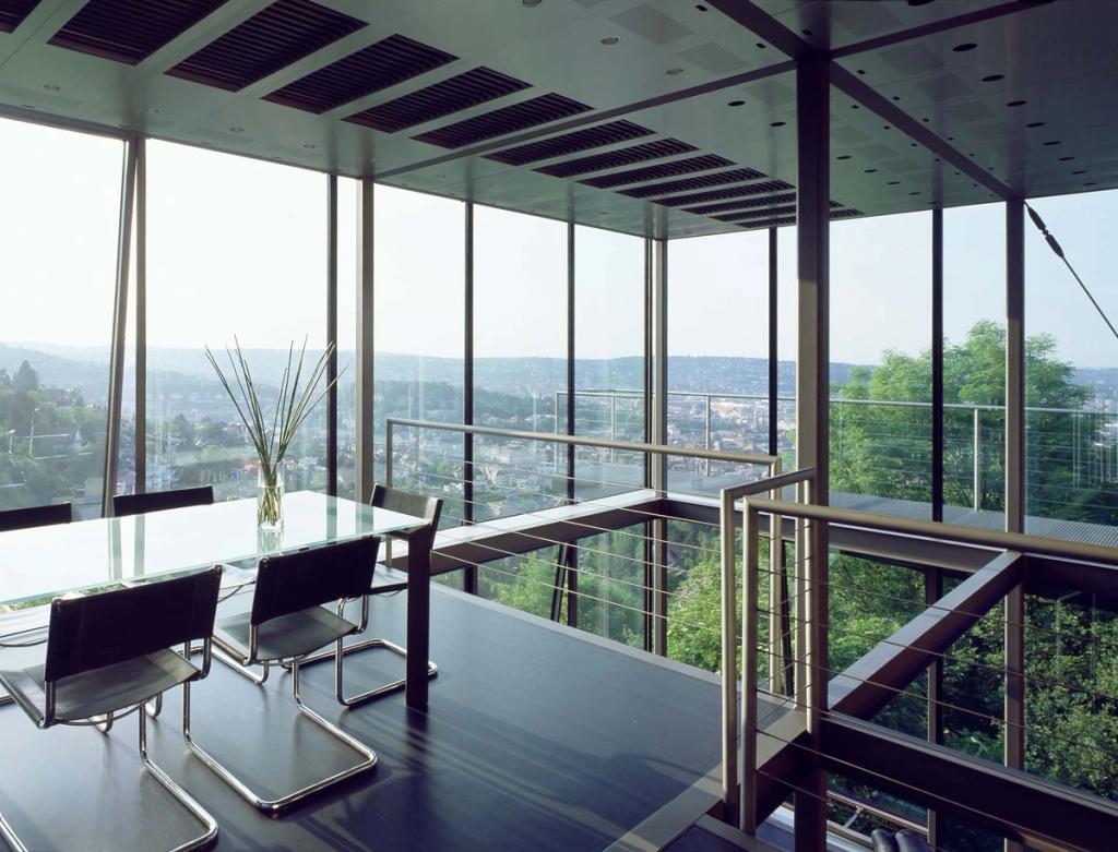 The dining area of house R-128, with a glass table and panoramic views of the hills