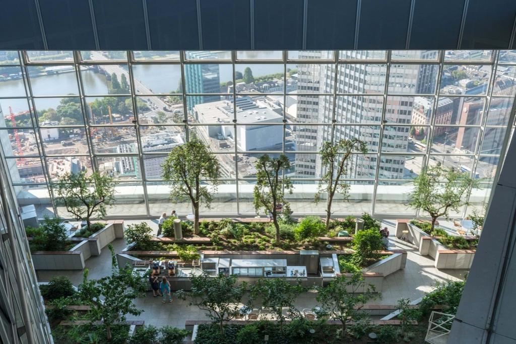 A landscaped winter garden with trees inside the Commerzbank Tower, with a panorama of Frankfurt visible through the glass