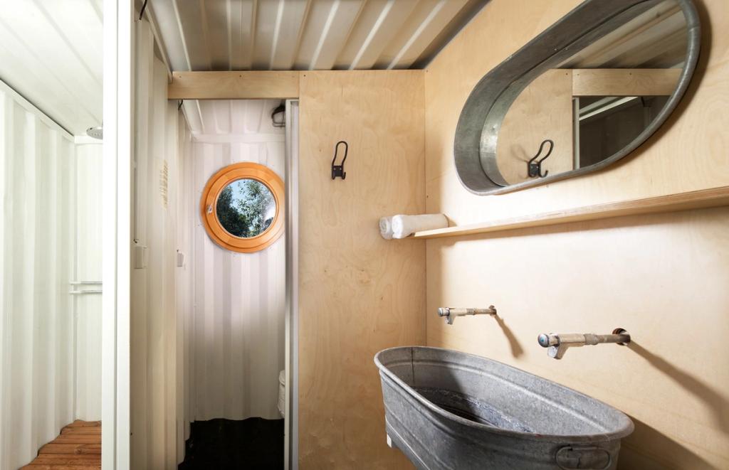 Санузел Containhotel с фанерными стенами, круглым иллюминатором и оцинкованным корытом-раковиной