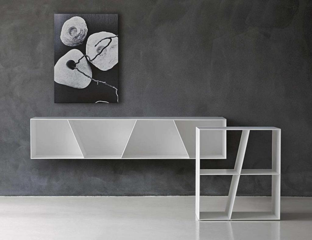 White X-shaped shelving unit for B&B Italia against a dark concrete wall with a photograph of stones