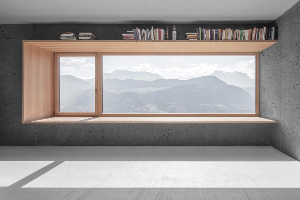 A panoramic wooden window with views of the Alps and a bookshelf above it