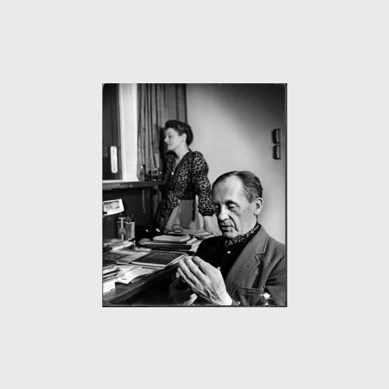 Walter Gropius examining photographs at his desk, a woman standing in the background