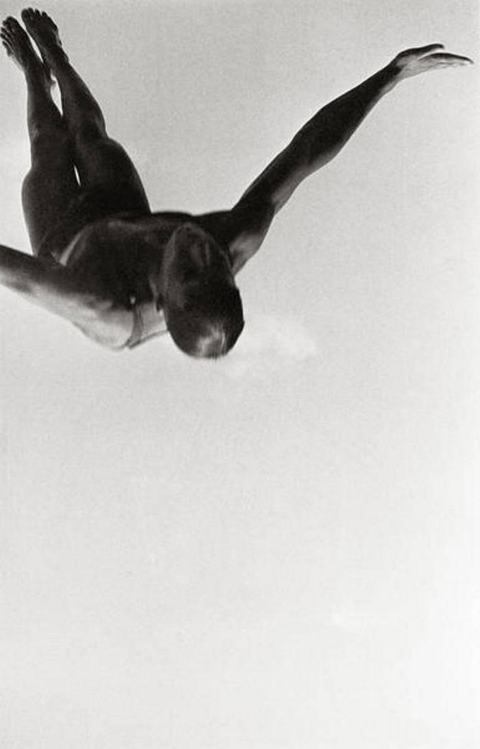 A diver in mid-air against a bright sky, photographed from below