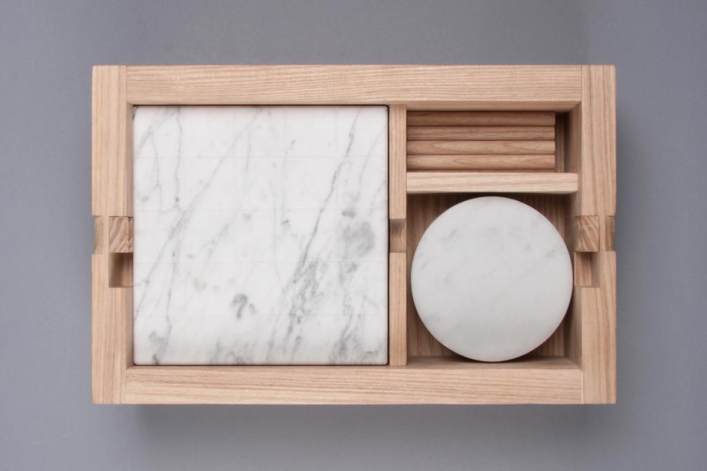 A wooden tray organiser with white marble inserts — one square and one circular — designed by Lyosha Galkin