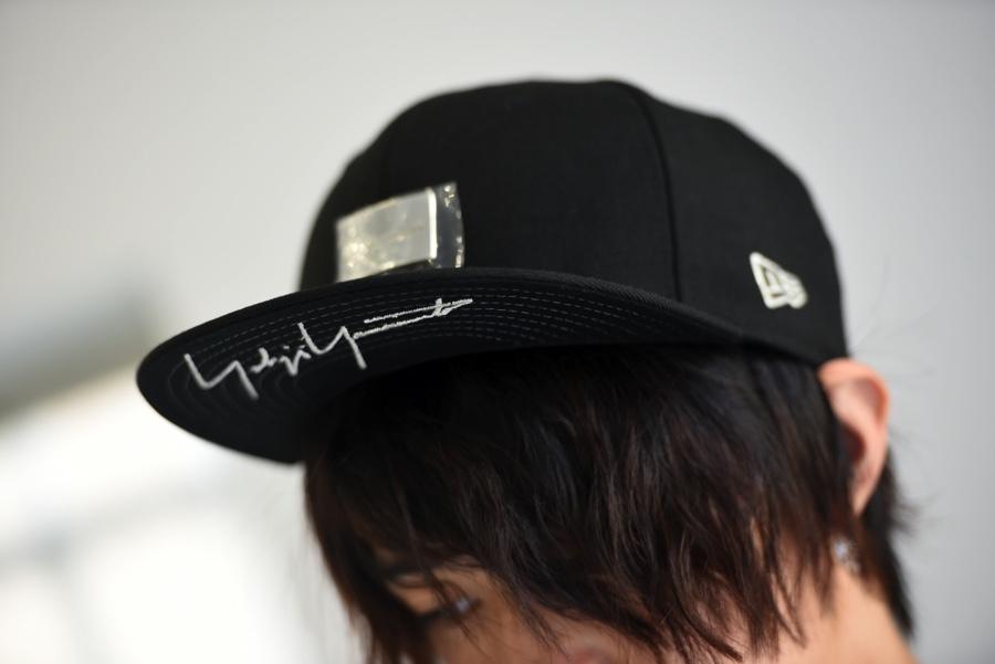 A black New Era baseball cap with an embroidered Yohji Yamamoto signature on the brim