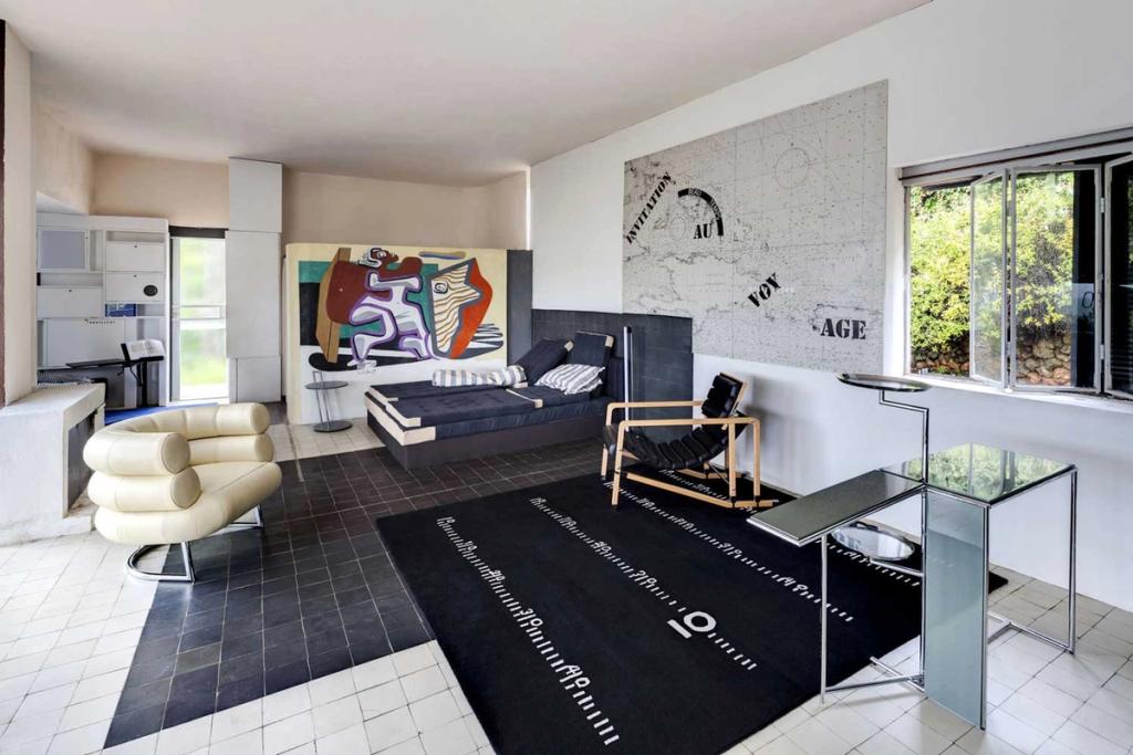 Living room of Villa E-1027: a Bibendum armchair, a daybed, a map fresco on the wall and a dark rug with inscriptions