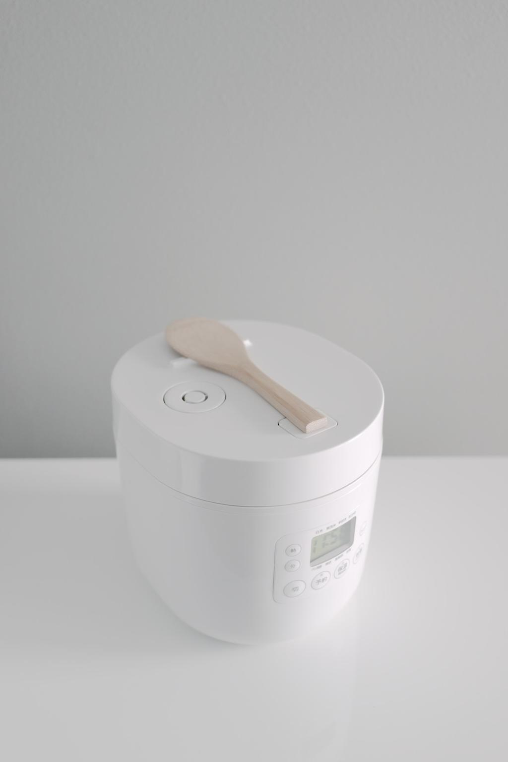 A white rice cooker with a wooden spatula resting on the lid