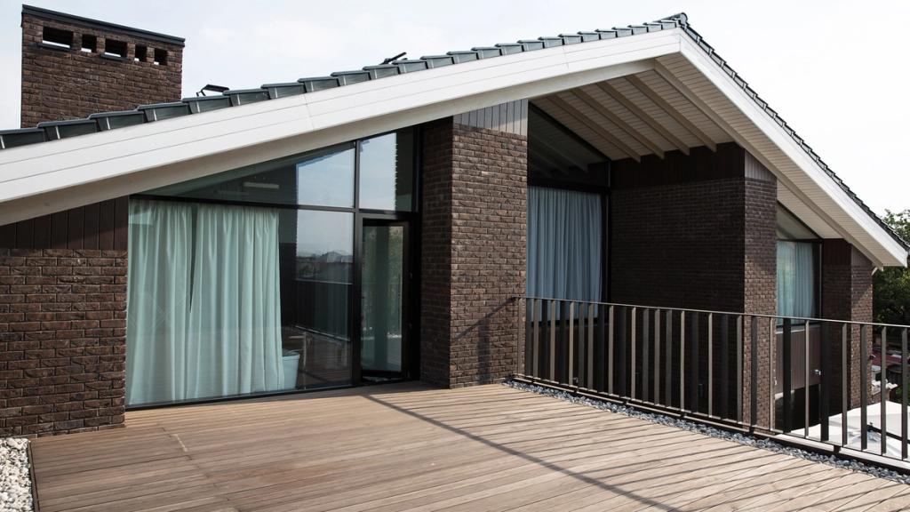 An open rooftop terrace with wooden decking, a brick chimney stack and panoramic glazing