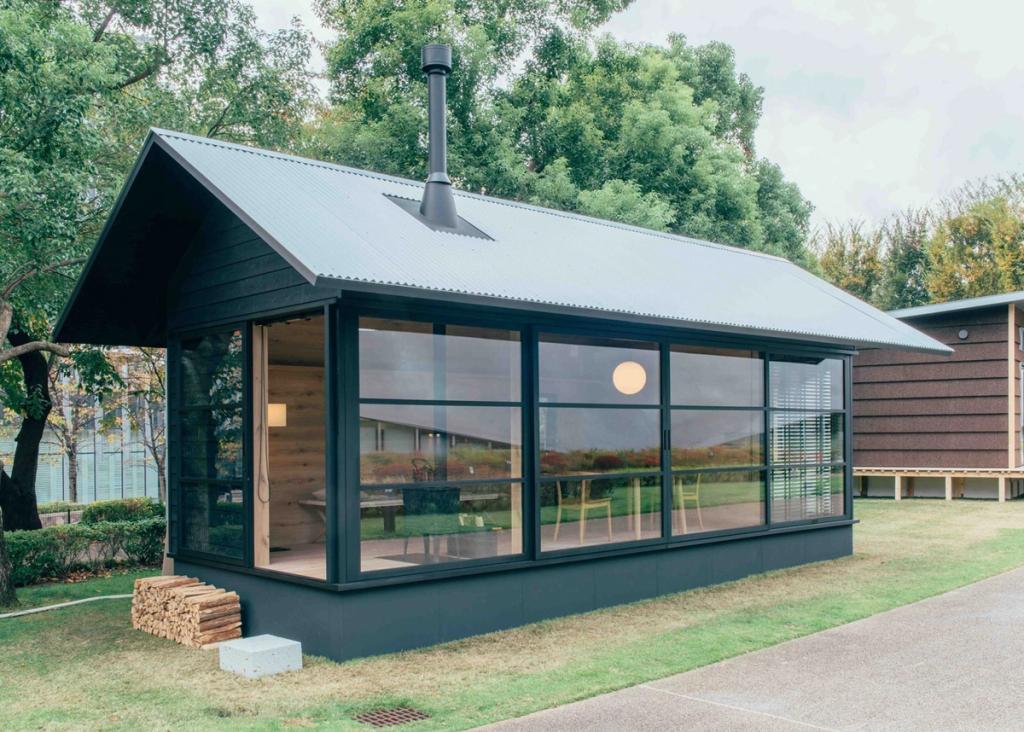 MUJI Hut: a compact dark cabin with a pitched roof and large windows set on a lawn
