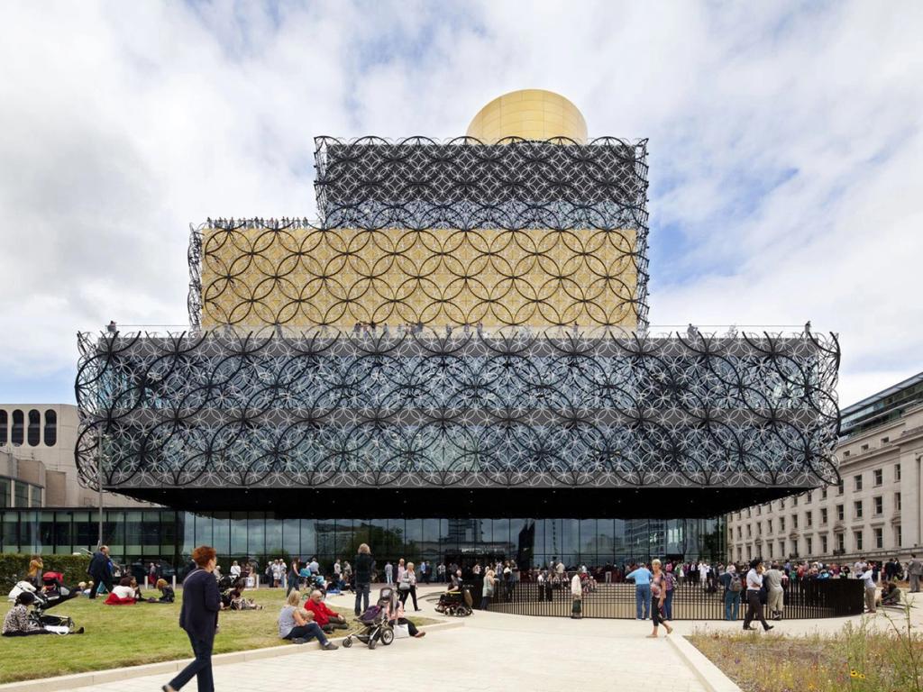 The stepped facade of the Library of Birmingham with a black-and-gold filigree pattern and a gold cylinder at the top