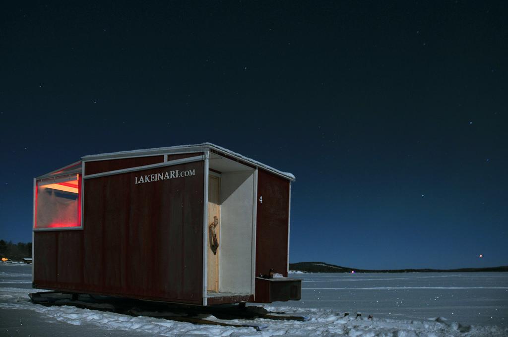 Красный домик Lake Inari на полозьях с открытой дверью под звёздным небом