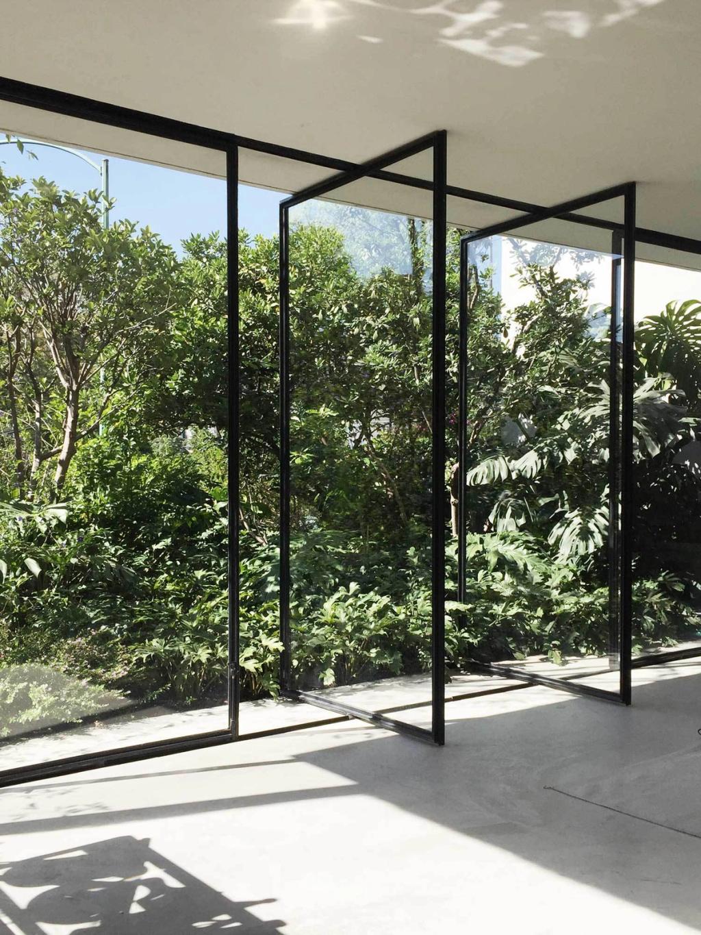 An empty room with pivoting glass walls opened onto a lush green garden