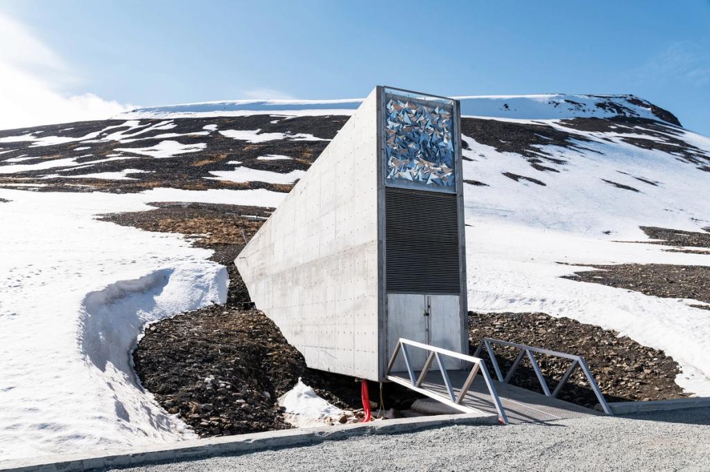 The concrete wedge of the vault with its mirrored mosaic above the entrance, surrounded by partly melted snow beneath a blue sky