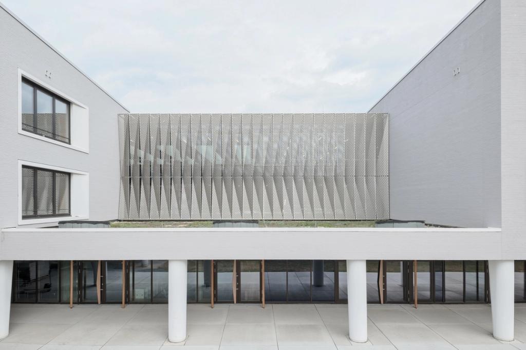 Hessenwald school: a white volume with a perforated metal façade raised on columns