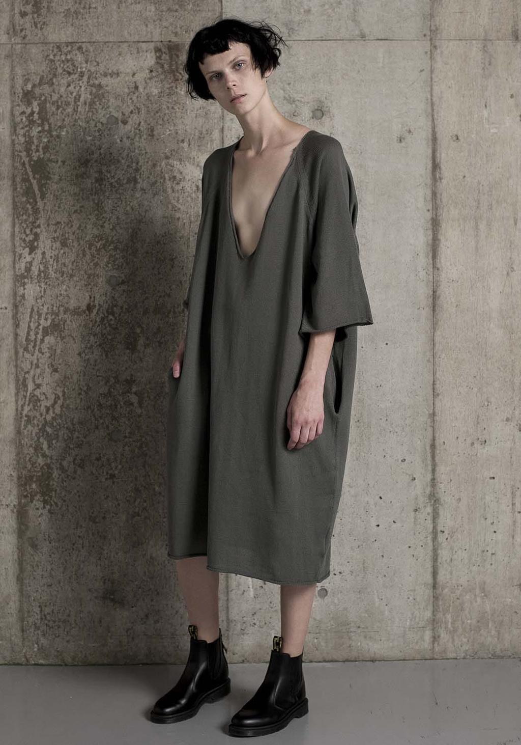 A model by a concrete wall in an oversized khaki dress with a deep neckline