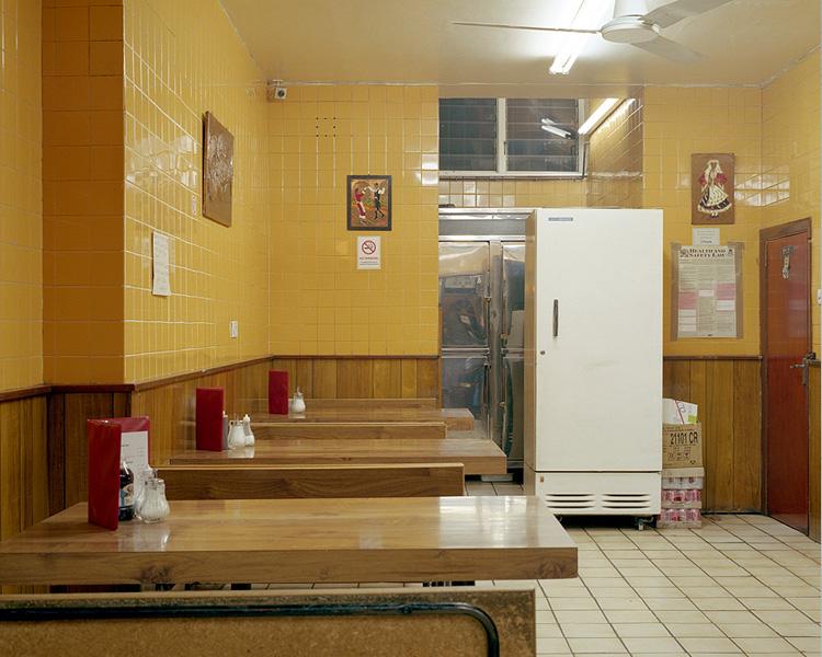 A diner with yellow tiled walls, wooden tables and a white refrigerator by the entrance