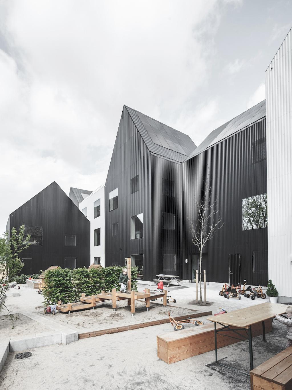 The courtyard of the COBE Architects kindergarten with its black houses, a sandpit, wooden tables and children's bicycles