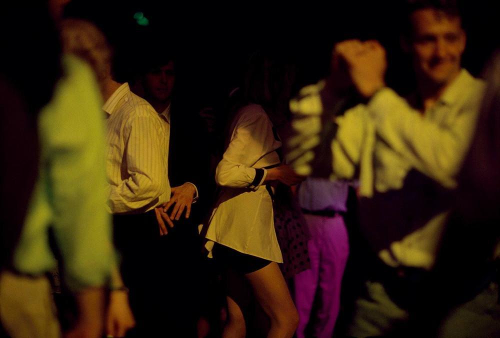 Young people dancing in the half-dark of a club beneath yellow and pink lights