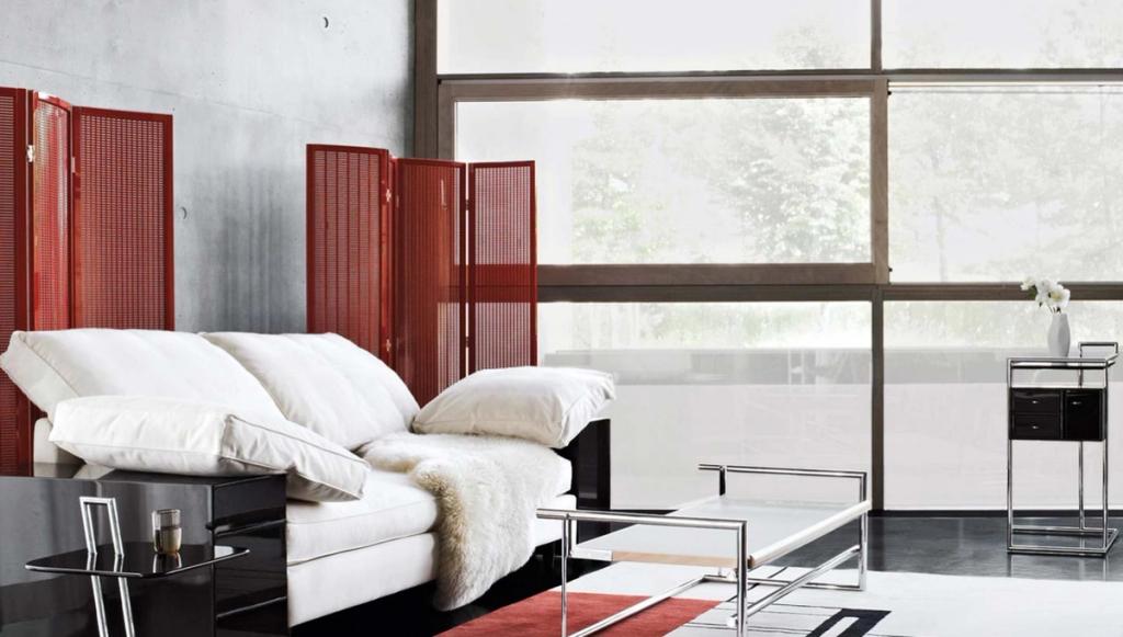 A white sofa with cushions behind a red perforated screen by a panoramic window