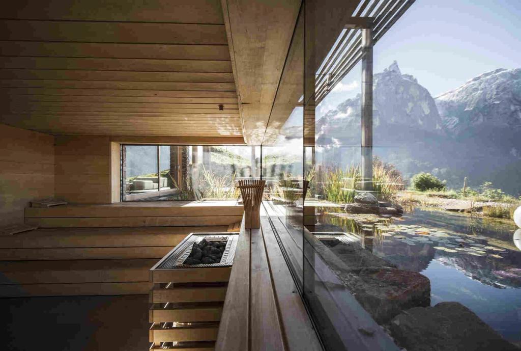 A wooden sauna with a panoramic window overlooking the Dolomite Alps and a natural pond