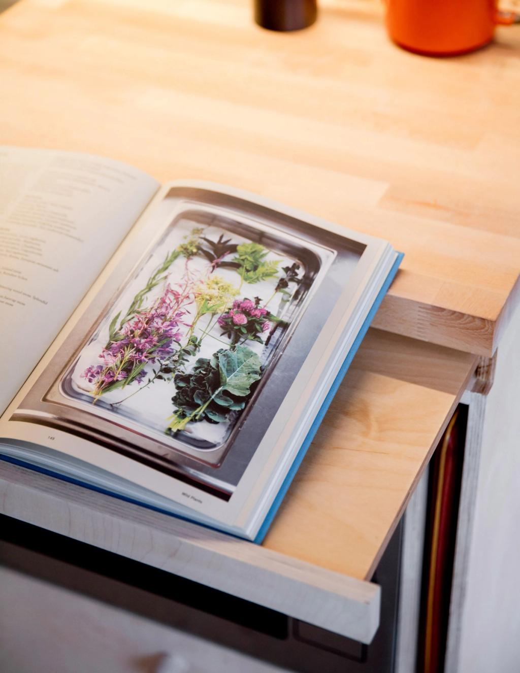 Раскрытая книга с фотографией полевых цветов лежит на выдвижной фанерной столешнице