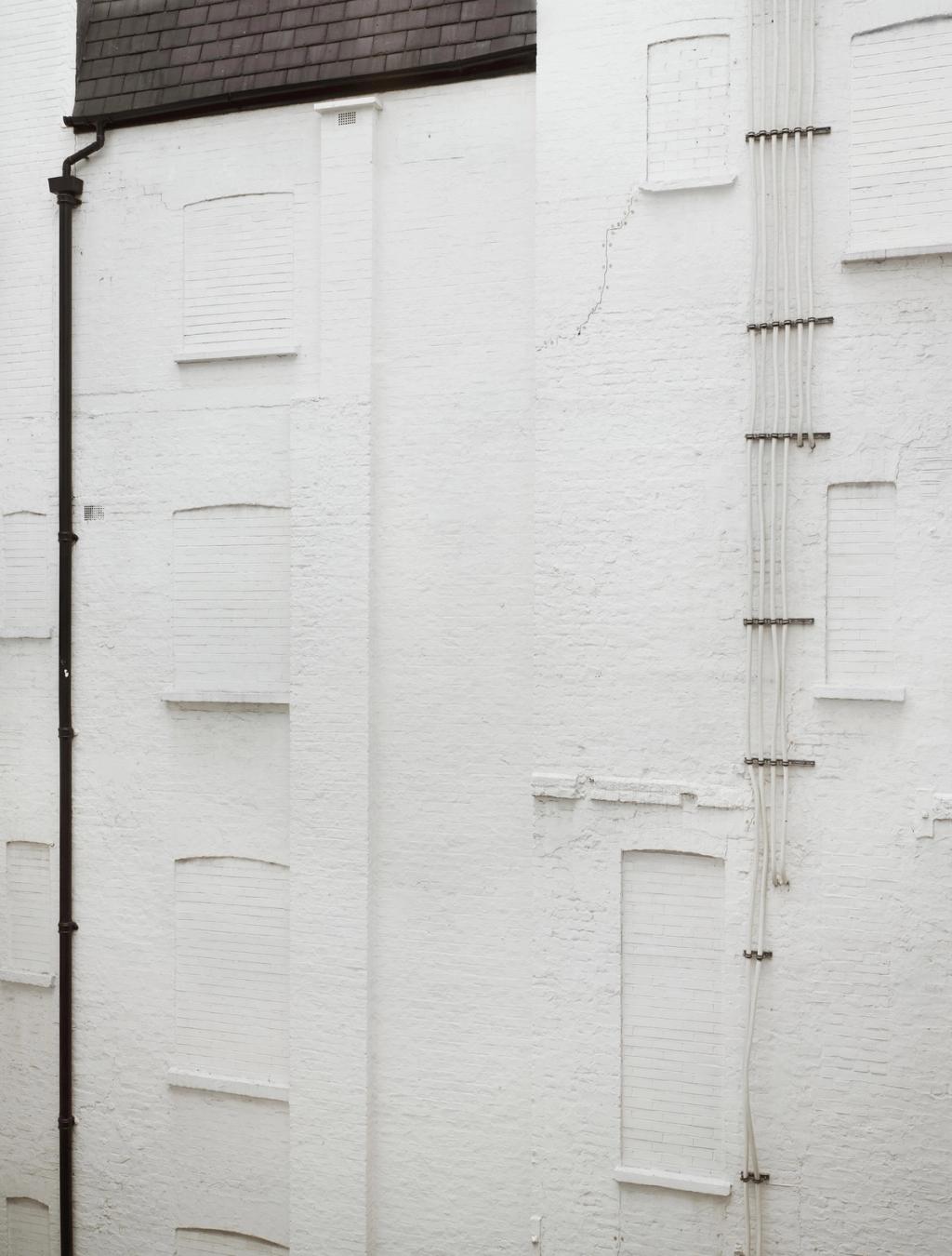 A blank white plastered wall with bricked-up windows and a bundle of cables