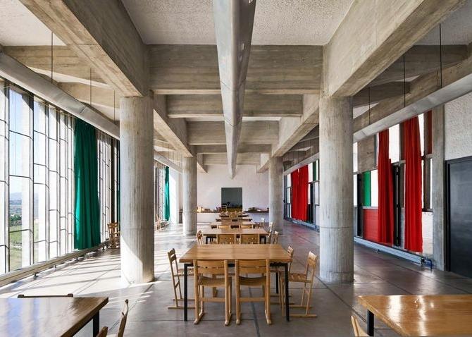 The refectory of Couvent Sainte-Marie de La Tourette with wooden tables and coloured curtains