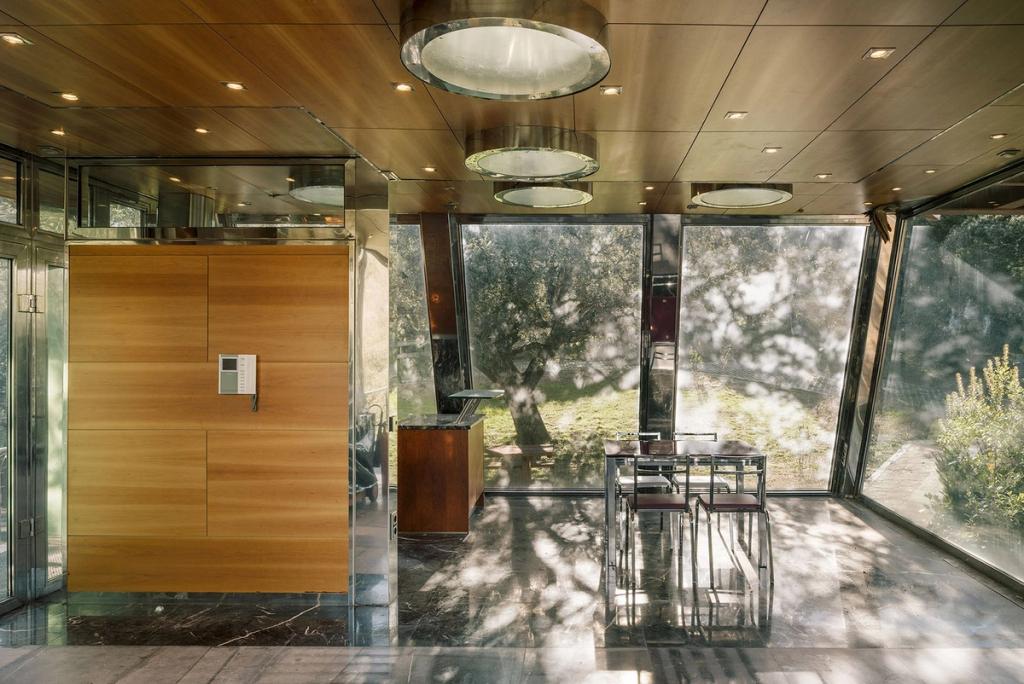 A dining room with glass walls, round skylights and views of the trees