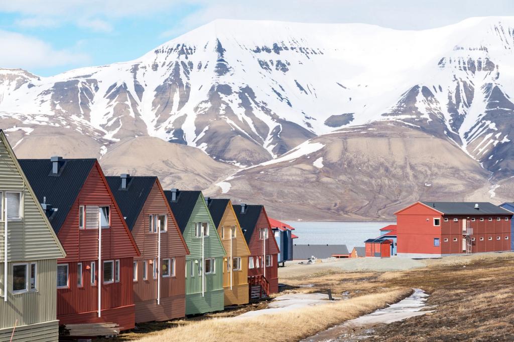 A row of red and green wooden houses in Longyearbyen against a backdrop of snow-capped mountains and a fjord