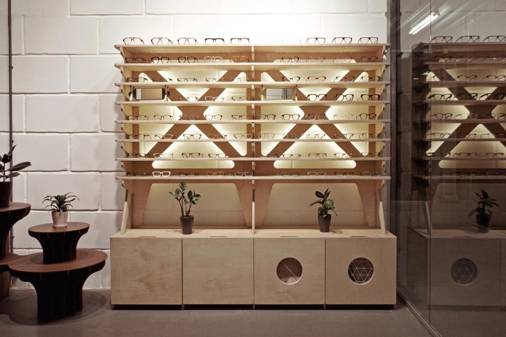 An illuminated plywood shelving unit displaying glasses in an optician's interior with a brick wall