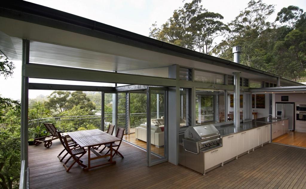An open timber deck with a kitchen and grill set against a green hillside