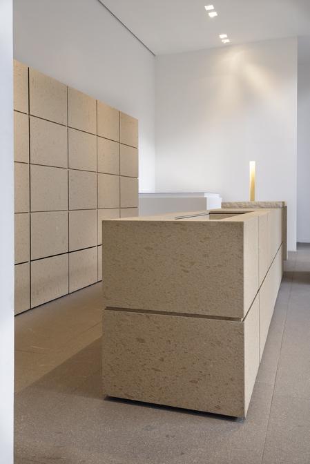 A minimalist interior featuring a massive stone counter and a wall clad in pale limestone slabs