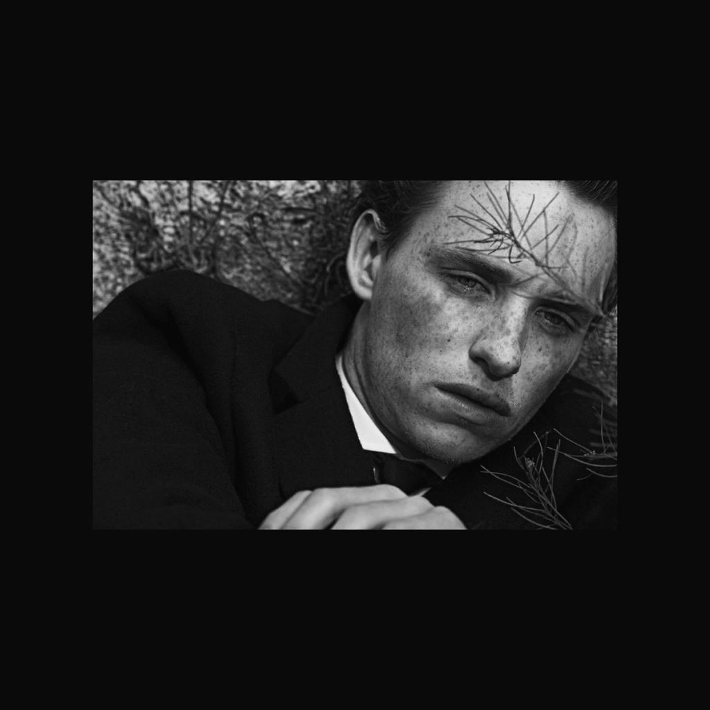 A young man in a dark jacket lies on the ground among dry branches