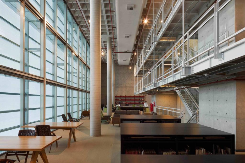 The reading room of the Brasiliana Library, featuring concrete columns, a glass wall and wooden tables