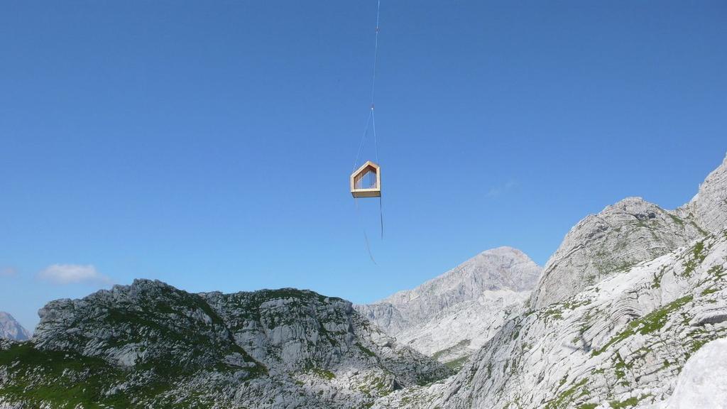 Модуль убежища Alpine Shelter Skuta висит на тросе высоко в горах Словении на фоне синего неба